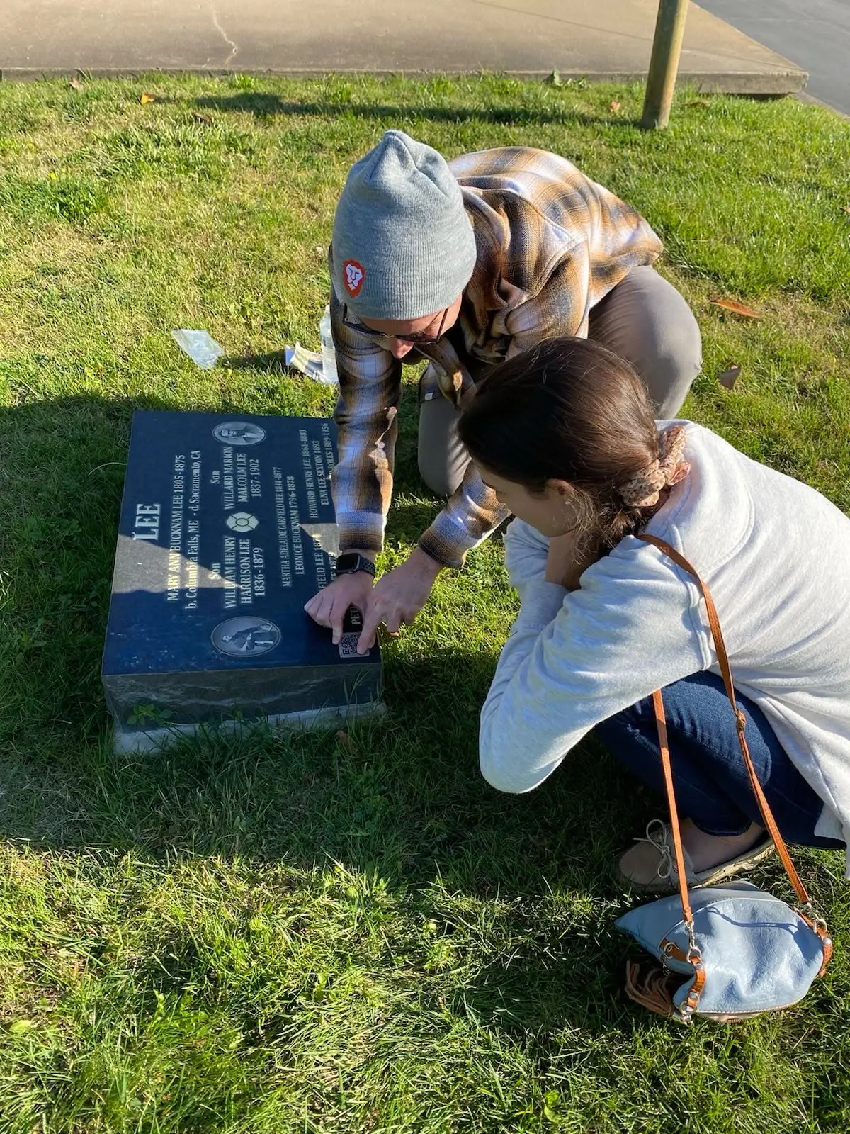 Ryan and a family member kneeling in the grass, pressing a QR code marker onto the Lee family headstone